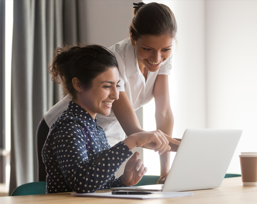 Dwie uśmiechnięte kobiety wskazują dłonią na ekran laptopa